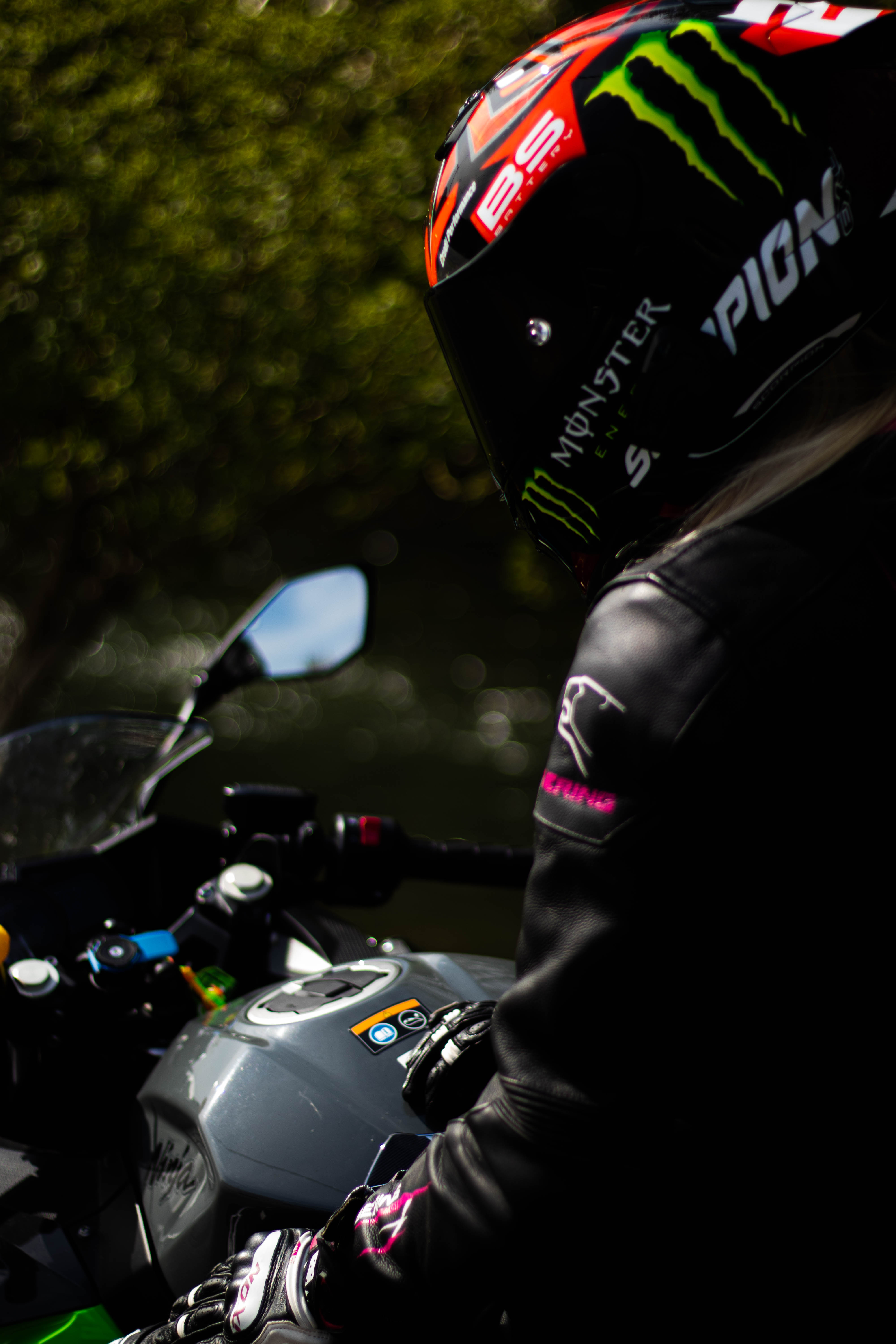 Photo d'une motarde assise sur sa moto trois quart dos avec la visière baissée